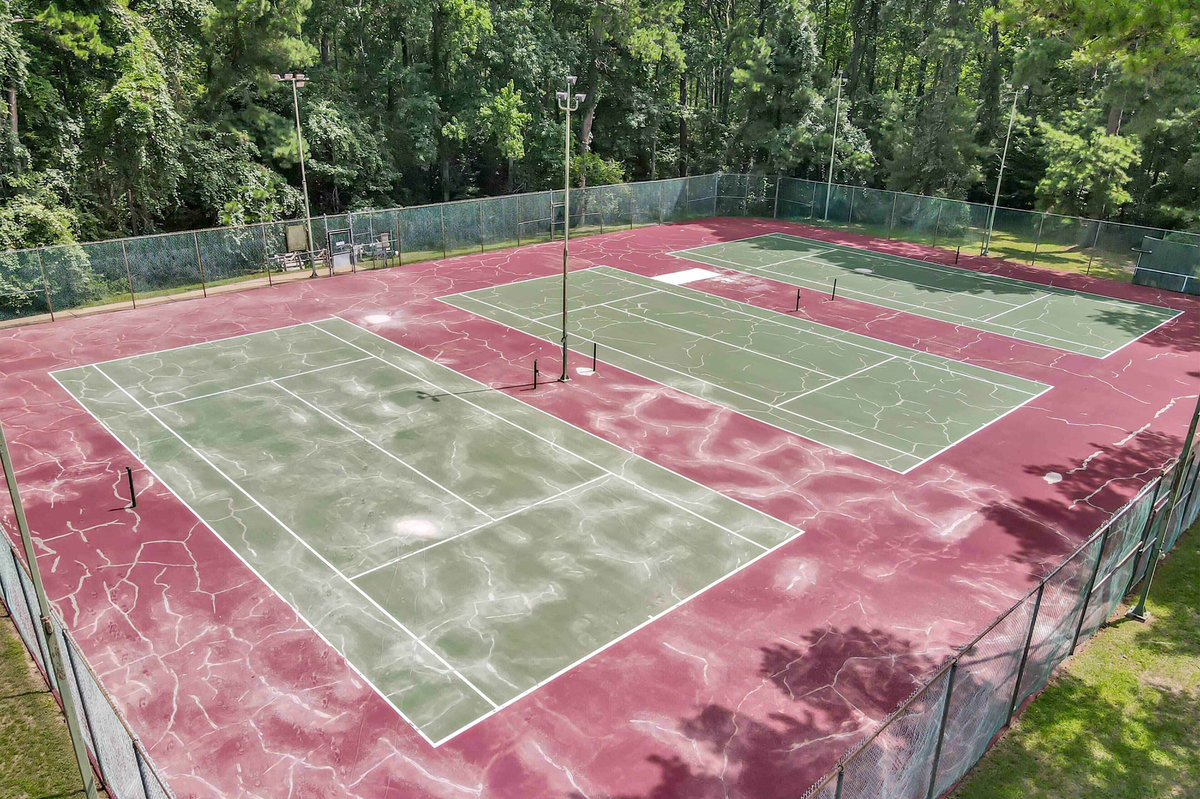 Una cancha de tenis con superficie verde y roja, rodeada por una valla de metal y árboles.