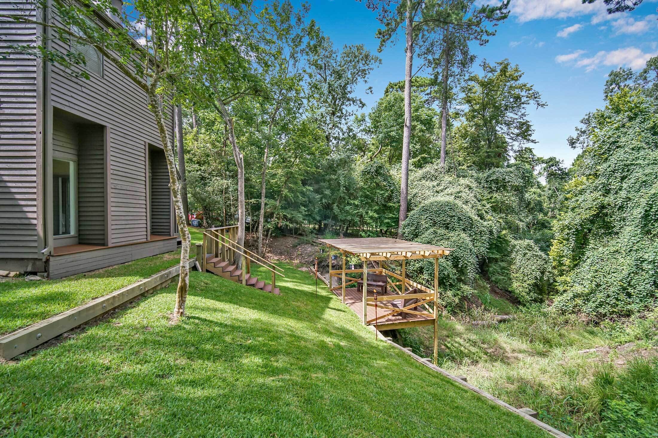 A modern house with a wooden deck, a staircase leading to a covered outdoor area, and a lush garden.