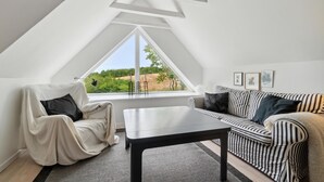 A modern loft bedroom with a sloped ceiling, a large window offering a view of greenery, a striped sofa, a chair, and a small table. - Stunning home in Hasle with WiFi (Hasle)