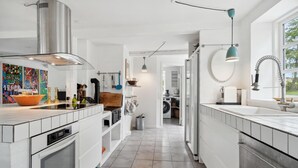 A modern kitchen with white cabinetry, a stainless steel range hood, and a large island with a bowl. There is a view into the adjacent laundry area. - Stunning home in Hasle with WiFi (Hasle)