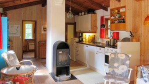 A cozy cabin interior with a fireplace, wooden cabinets, a dining area with chairs, and a kitchen with basic appliances. - 2 bedroom awesome home in Nexø (Nexø)