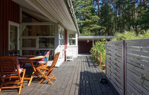 Een houten terras met buitenmeubilair, een wit hek en uitzicht op een bebost gebied.
