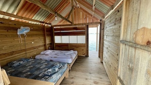 Eine Holzhütte mit zwei Betten, einem Ventilator und Blick auf das Wasser.