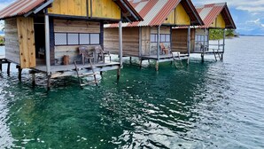 Wasserbungalows mit Holzbauten und Metalldächern, verbunden durch Wege über klares Wasser.