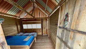 Eine Holzhütte mit geneigtem Dach, zwei Betten mit blauer Bettwäsche und einem kleinen Tisch.