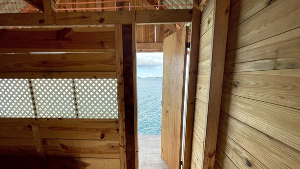 Eine Holzhütte mit einem Bett, einem Fenster mit Gittermuster und Blick auf das Wasser.