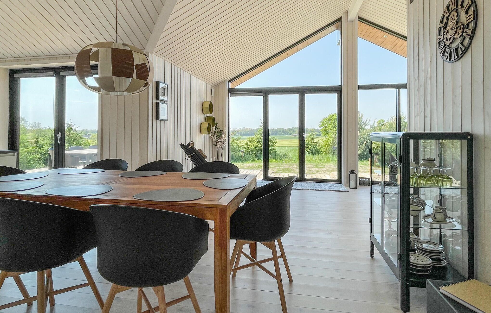 A dining area with a wooden table and black chairs, large windows, and a view of greenery.