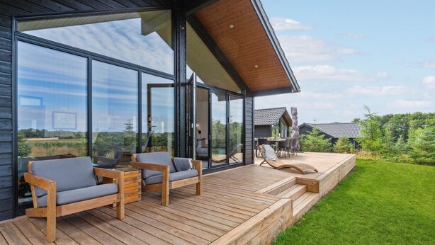 Une terrasse extérieure moderne, dotée de meubles en bois et de portes vitrées donnant sur un patio abrité.