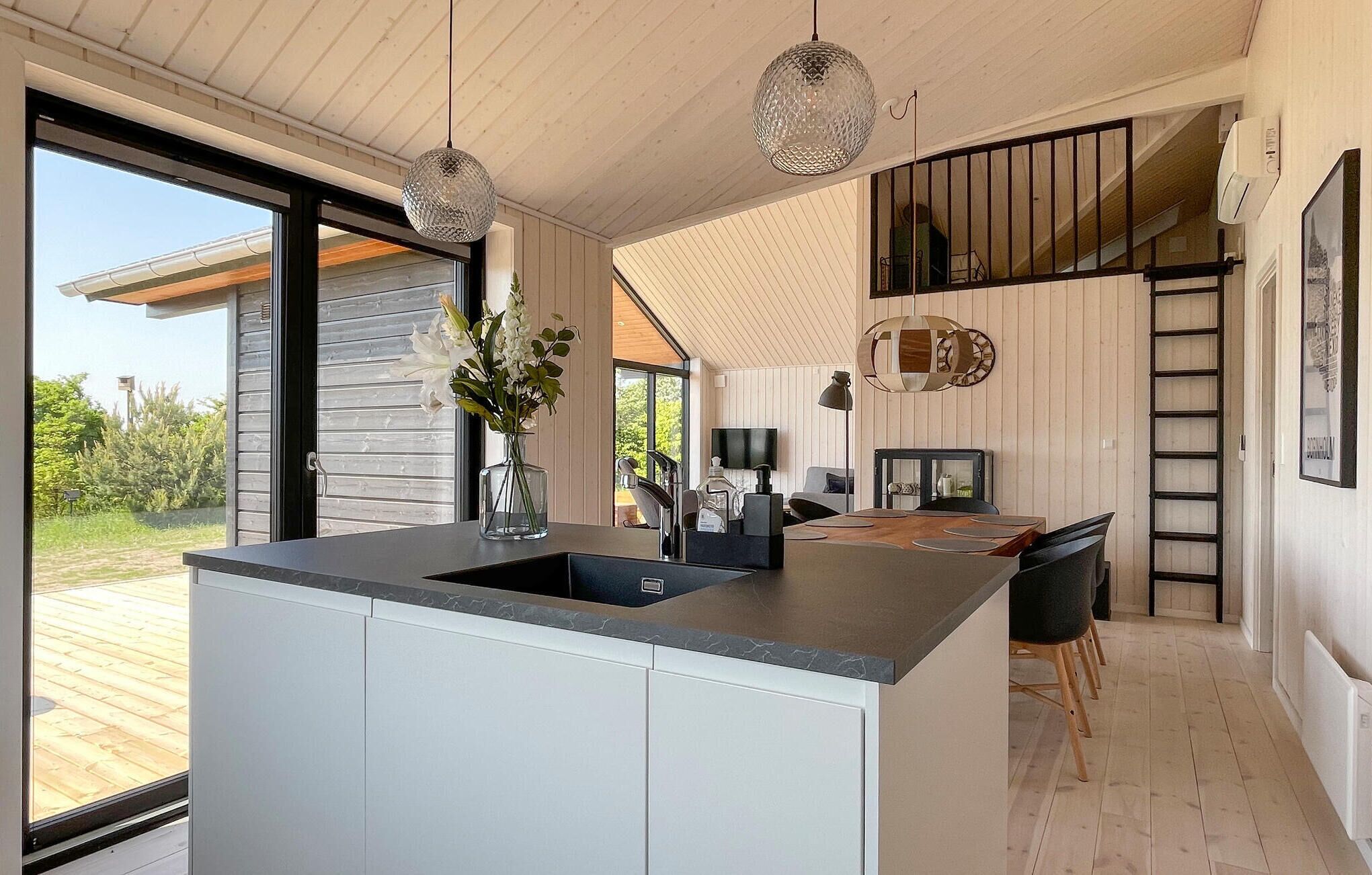 Une cuisine moderne dotée d’un grand îlot central, d’un coin repas avec une table en bois et offrant une vue sur l’extérieur.