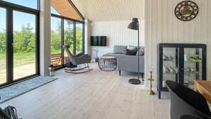 Un salon moderne doté d’une grande fenêtre, d’un canapé gris, d’un fauteuil à bascule et d’un meuble avec des portes en verre.