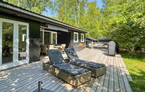 A wooden deck with outdoor furniture, a covered grill, and a glass-enclosed patio area. - Amazing home in Aakirkeby (Aakirkeby)