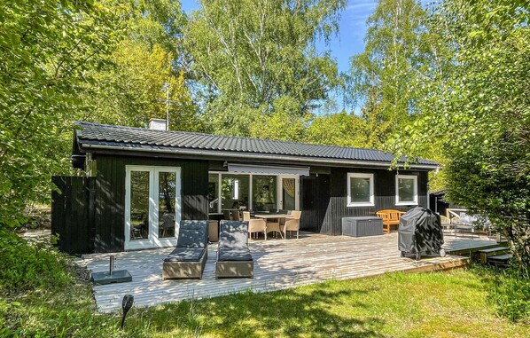 A wooden cabin with a deck, outdoor seating, and a grill. - Amazing home in Aakirkeby (Aakirkeby)