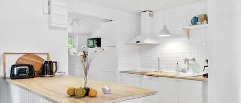 A modern kitchen with white cabinetry, a wooden countertop, and a central island with decorative pumpkins and a vase.