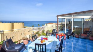 Une terrasse sur le toit, avec une table dressée pour le dîner, des chaises, des plantes en pot et une vue sur la mer.