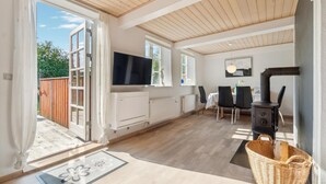 A spacious living area with a wooden ceiling, a TV mounted on the wall, a dining table with chairs, a fireplace, and a large window providing a view of the outdoors. - 2 bedroom awesome home in Nexø (Nexø)