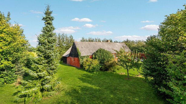 A rustic barn with a sloped roof surrounded by lush greenery and trees. - 2 bedroom awesome home in Nexø (Nexø)