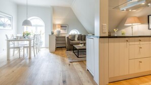 A modern kitchen with a glass range hood, a dining area with a white table and chairs, and a cozy living space with a sofa and a coffee table. - Witthüs, Whg. 19 - Witthüs (Wenningstedt-Braderup (Sylt))