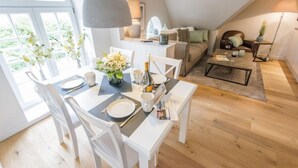 A dining area with a table set for two, a chandelier, and a view of a living area with a sofa and a coffee table. - Witthüs, Whg. 19 - Witthüs (Wenningstedt-Braderup (Sylt))