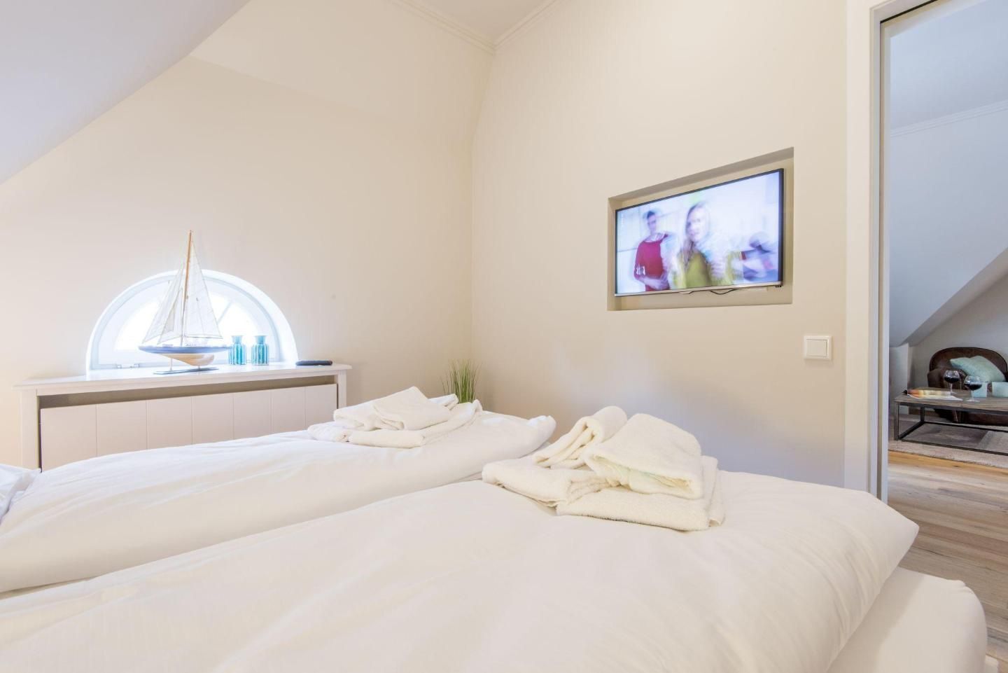 Quarto de hotel com duas camas, decoração náutica com um veleiro, televisão na parede e vista para o exterior.