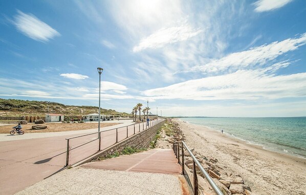 A coastal walkway with a metal railing, a clear sky, and a beach in the background.
