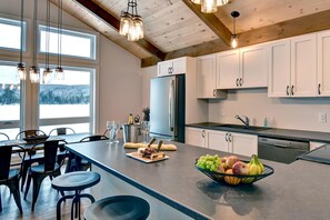 A modern kitchen with a large island, white cabinets, and a view of a snowy landscape through large windows. - Beautiful waterfront cottage (Labelle)