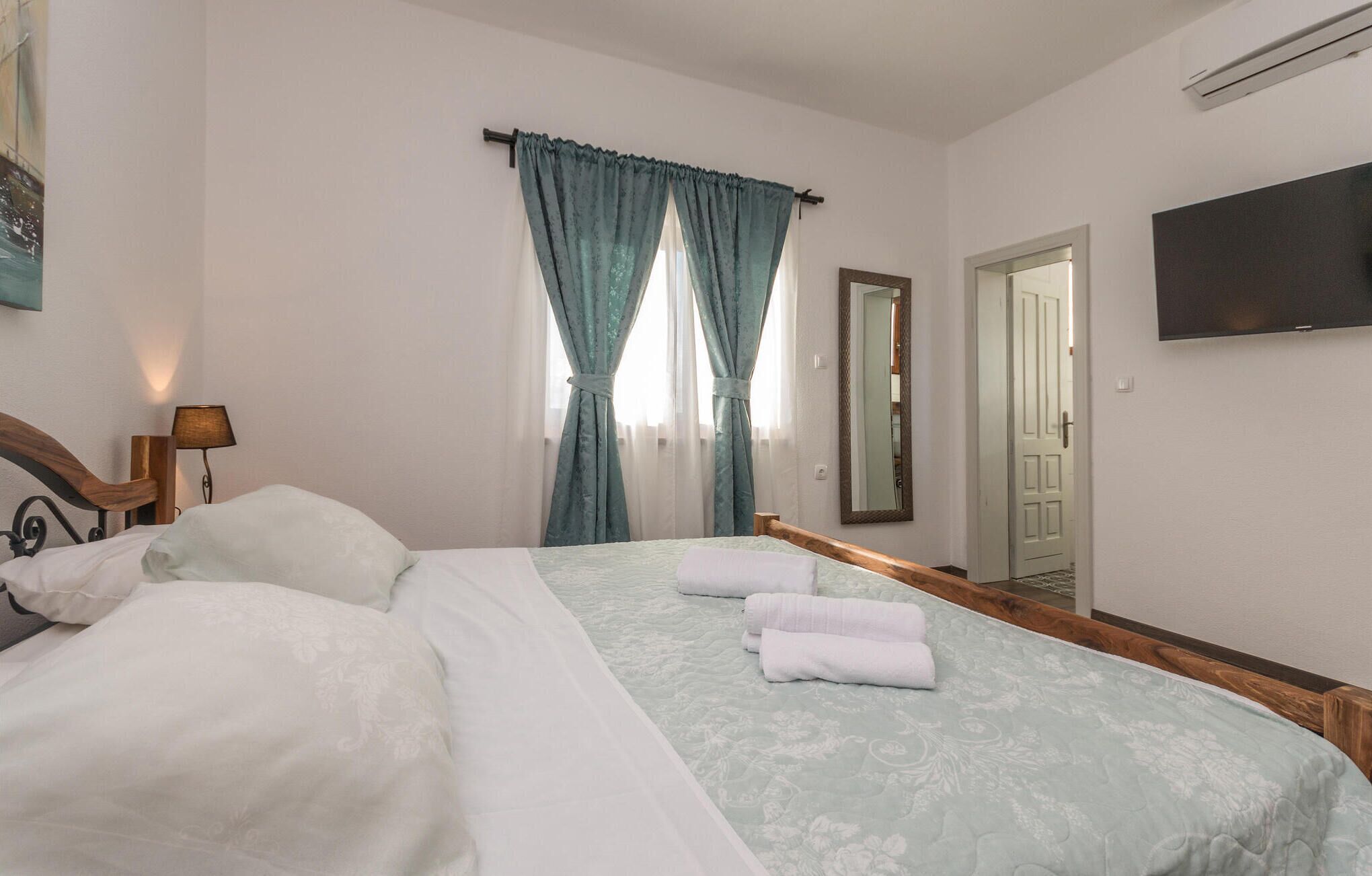 A hotel room with a bed, a bedside lamp, a television, and a window with curtains.