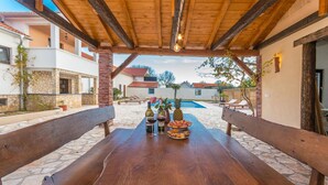 Ein Holztisch auf Steinboden, umgeben von Steinmauern und einer Holzpergola.