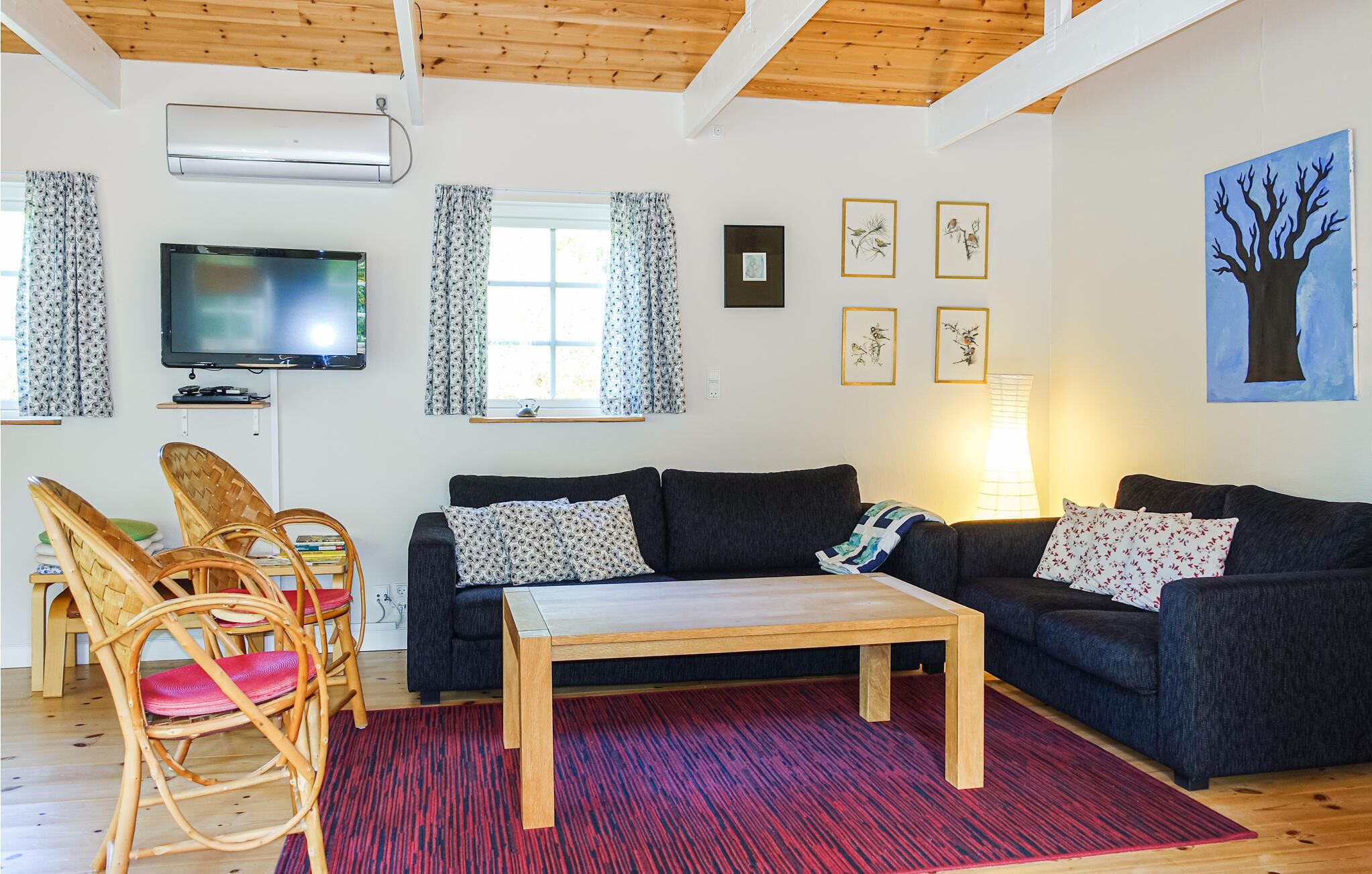 A living room with a dark sofa, a wooden coffee table, wicker chairs, a flat-screen TV, and artwork on the walls.