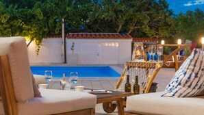 An outdoor seating area with a pool, wooden furniture, and a table set with wine glasses and bottles. - Pet friendly home in Nin (Nin)
