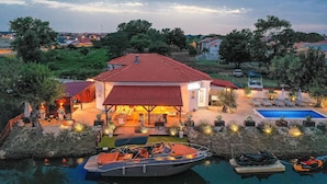 A house with a swimming pool, a boat docked in the water, and a patio area with lounge chairs. - Pet friendly home in Nin (Nin)