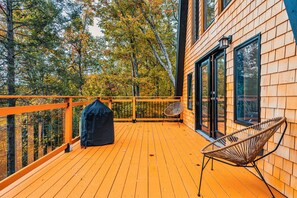 Enjoy outdoor dining and relaxation on this deck with a grill and seating area, offering views of the surrounding forest.