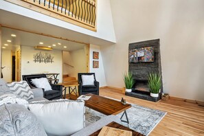 A modern living room with a fireplace, a high ceiling, and a view of the outdoors.