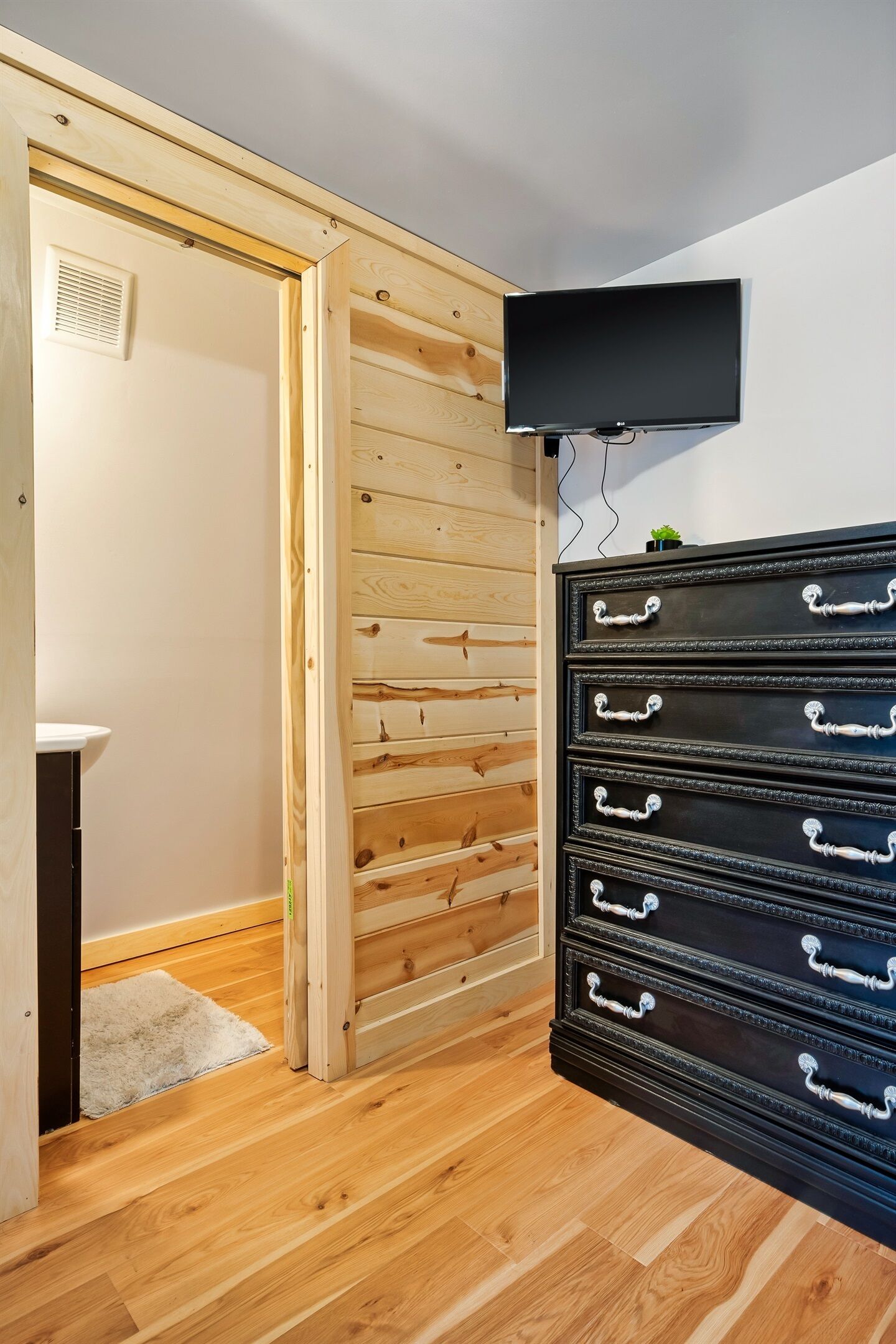 Een kamer met een houten wandpaneel, een zwarte dressoir met meerdere lades en een flatscreen televisie die aan de muur is bevestigd.