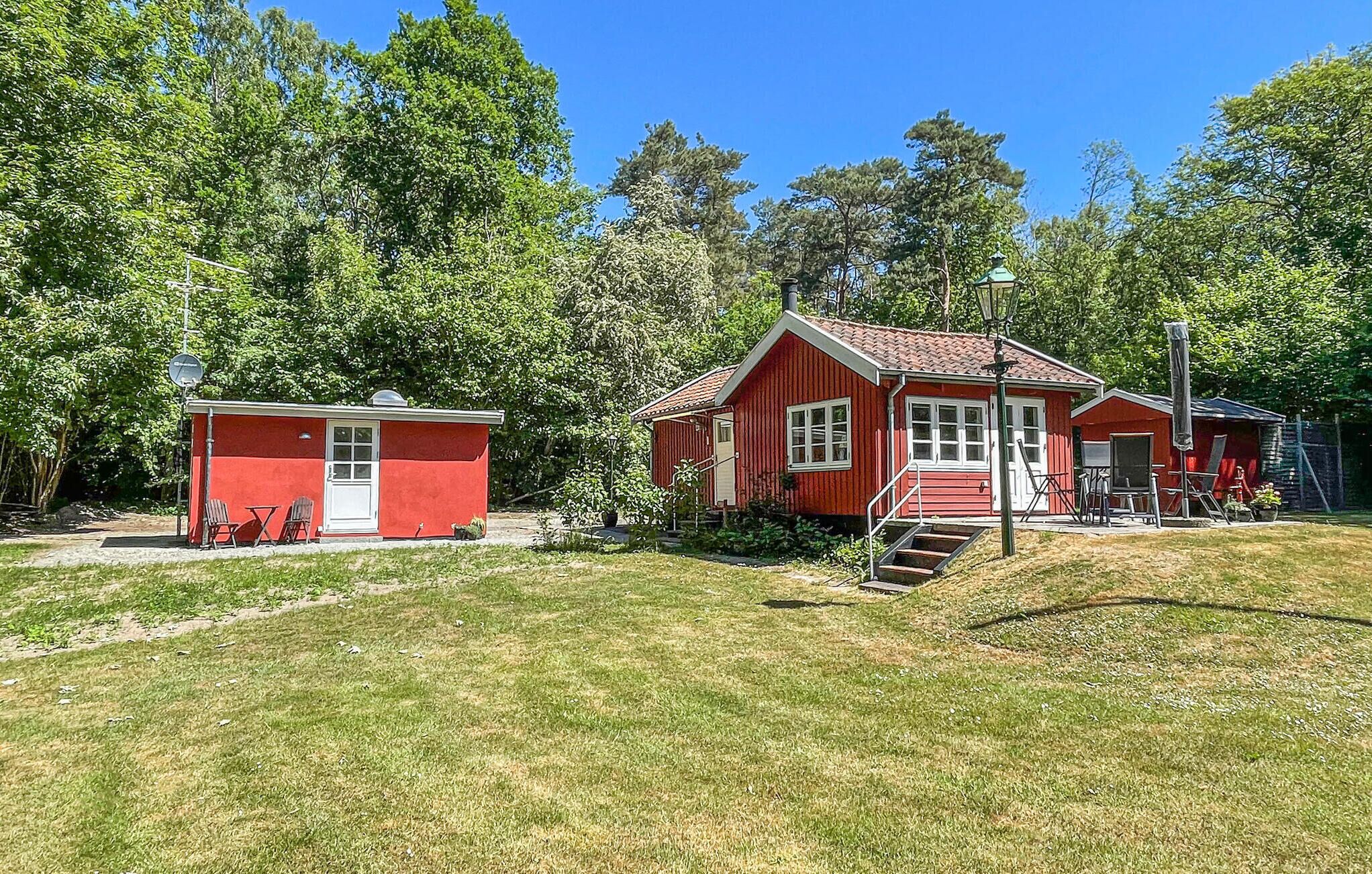A red wooden cabin with a small attached shed, surrounded by trees and a grassy area.