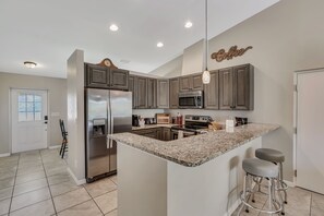 A modern kitchen with granite countertops, stainless steel appliances, and bar stools.