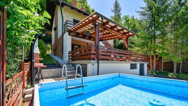 Ein Swimmingpool mit Holzterrasse und Treppe zu einem überdachten Bereich.