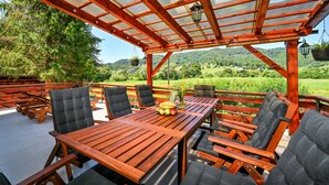 Eine Holzterrasse im Freien mit Tisch und Stühlen, einem hängenden Blumentopf und Blick auf eine grüne Landschaft.