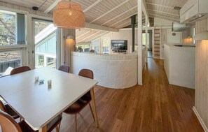 A modern kitchen with a central island, a dining area with a white table and chairs, and a large window providing natural light.