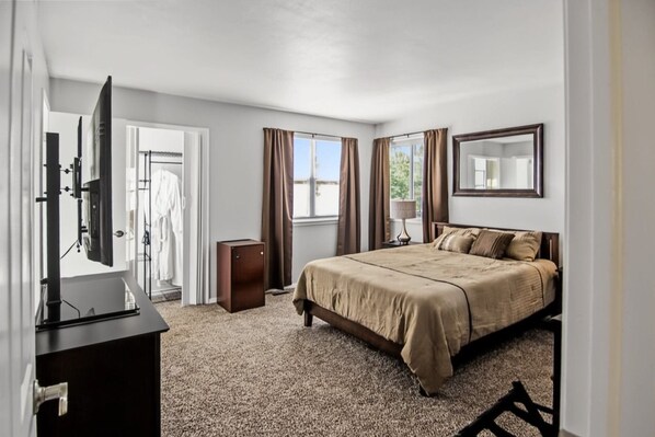 Habitación de hotel con cama, televisor, armario y ventana con cortinas.