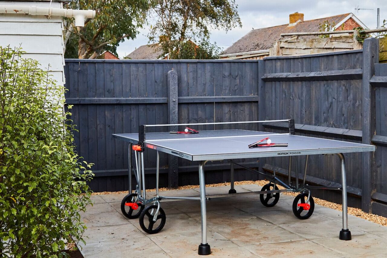 A ping pong table with wheels set up outdoors, likely in a backyard or patio area.