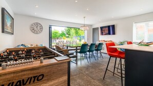 Een moderne keuken met een tafelvoetbaltafel, een eethoek met rode stoelen en een groot raam met uitzicht op de omgeving.