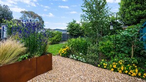 Een tuin met een grindpad, diverse planten en een houten plantenbak.