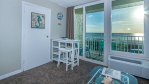 Una habitación con vista a la playa, una puerta blanca, una mesa pequeña con un cuenco, una silla y un ventanal grande.