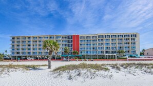 Un hotel de varios pisos con una sección vertical roja en el centro, balcones y ubicación frente a la playa.