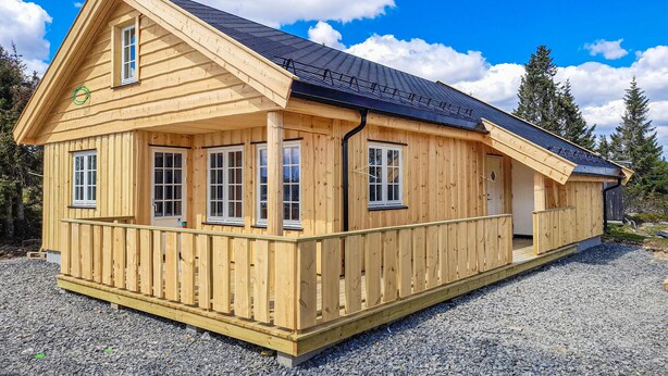 Eine Holzhütte mit Satteldach, zahlreichen Fenstern und einer Schotterzufahrt.