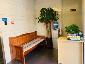 A wooden bench with a striped cushion, a potted plant, and a reception desk with a sign. - Green Tree Inn Beijing Xicheng District Dashilan Express Hotel (Beijing)
