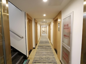 Ein Hotelgang mit einem zebraartig gestreiften Teppich, Holztüren und einem Schild mit der Zimmernummer 119.