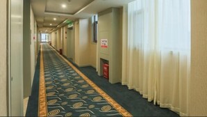 Un corridoio di un hotel con una moquette a motivi, un estintore e un cartello appeso al muro.