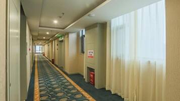 A hotel corridor with a patterned carpet, a fire extinguisher, and a sign on the wall.