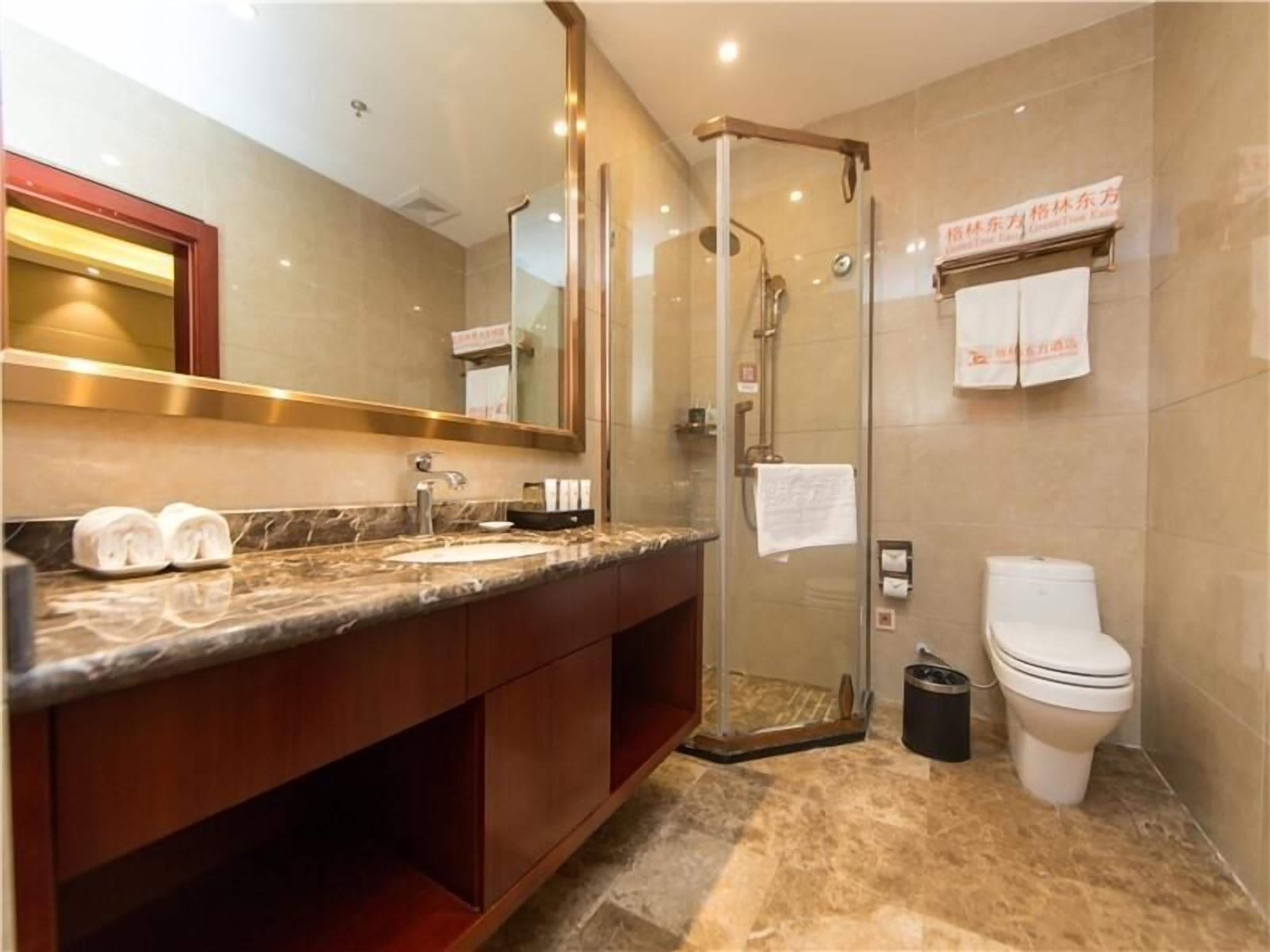 Un baño moderno con ducha envuelta en vidrio, lavamanos de mármol y un inodoro.